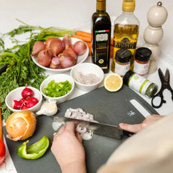 Person in a cooking class chopping onions on a cutting board with various ingredients and oils in the background